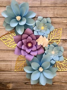 paper flowers are arranged on a wooden surface with gold leaves and other decorative items in the center