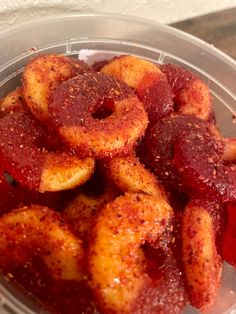 a plastic container filled with donuts covered in ketchup and seasoning sitting on top of a table