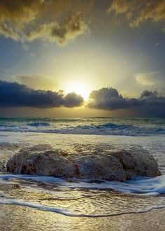 the sun is setting over an ocean with rocks in the foreground and waves on the shore