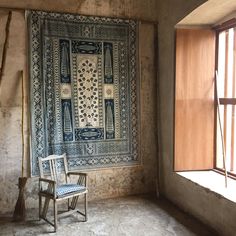 a chair sitting in an empty room next to a wall with a tapestry hanging on it