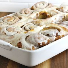 a white dish filled with cinnamon rolls on top of a wooden table