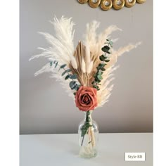 a vase filled with dried flowers and feathers on top of a white table next to a clock