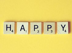 the word happy spelled with scrabble blocks on a yellow background, top view