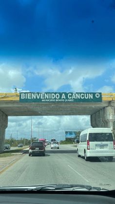 cars driving under an overpass on a highway with a sign that reads bienvenndo a cancun