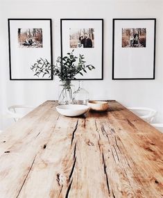 a wooden table topped with two white bowls filled with flowers next to pictures on the wall