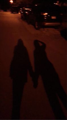 two people standing next to each other in the street at night with their shadows on the ground