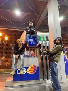 two men sitting on top of a parking meter next to another man standing in front of them