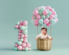 a baby sitting in a basket with balloons and the number 1 on it's side