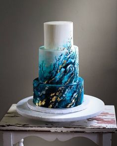 a three tiered blue and gold cake on a white plate