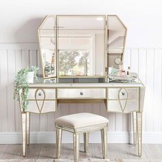 a dressing table with a mirror and stool in front of it on the floor next to a white wall