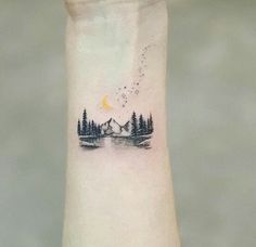 a small tattoo on the wrist of a person with trees and mountains in the background