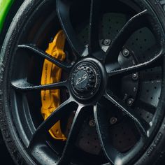 the front wheel of a green sports car with yellow brake pads and black rims