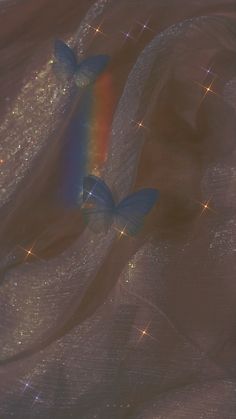 two blue butterflies flying in the sky with sparkles on it's wings and one has a rainbow colored tail