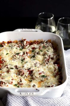 a casserole dish with cheese and meat in it on a towel next to two glasses