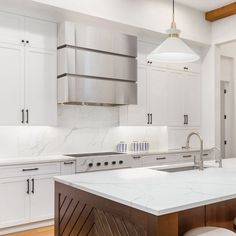 a kitchen with white cabinets and marble counter tops, along with an island in the middle