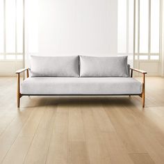 a white couch sitting on top of a hard wood floor next to two large windows