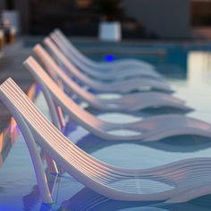 row of white benches sitting next to a swimming pool