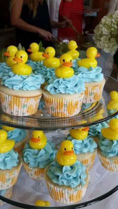 cupcakes with blue frosting and yellow rubber ducks on top are sitting on a glass platter