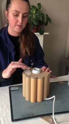 a woman is making something out of rolls of paper on a table with a plant in the background