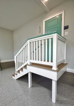 an empty room with white stairs and green door