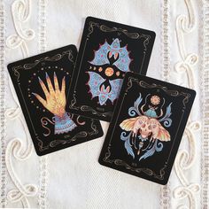 three playing cards with designs on them sitting on a white cloth covered tablecloth,