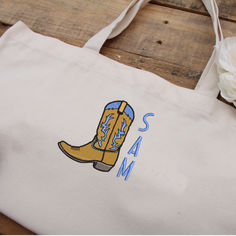 a white bag with a cowboy boot and name on it sitting next to a flower