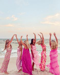 four women in long dresses standing on the beach with their hands up and arms raised