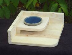 a wooden stand with a blue bowl on it's top and green plants in the background