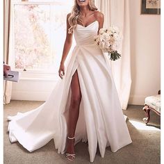 a woman in a white wedding dress standing next to a window with her legs crossed