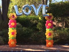 an arch made out of balloons with the word love spelled in large letters and flowers