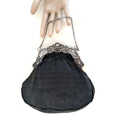 A black handbag with a Dutch 2nd standard silver (.833 purity), repousse frame with windmills, birds, a baby's face, and a cable chain handle.  The interior of the bag is hand sewn, taupe thick gauge, silk satin, and it has two small, side pockets.  The exterior silk is a finely ribbed matte black silk.  The handle drop is 3 1/2 inches, its overall dimensions are 7 1/2 H x 7 1/2 W x 1/2 D inches.  The bag dates from the late 19th to the first half of the 20th century. CONDITION:  Some signs of w Classic Silver Shoulder Bag With Chain Strap, Classic Silver Bag With Chain Strap, Silver Handheld Evening Bag With Chain Strap, Handheld Silver Evening Bag With Chain Strap, Classic Silver Shoulder Bag For Formal Occasions, Classic Silver Shoulder Bag For Formal Events, Elegant Evening Bag With Palladium Hardware For Formal Events, Elegant Formal Evening Bag With Palladium Hardware, Silver Shoulder Bag With Silver-tone Hardware As Gift