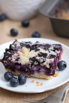 a piece of blueberry cheesecake on a white plate with fresh blueberries around it