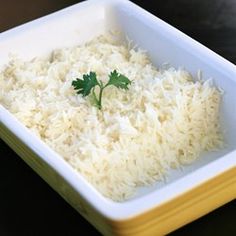 white rice with parsley in a yellow and white square dish on a black table