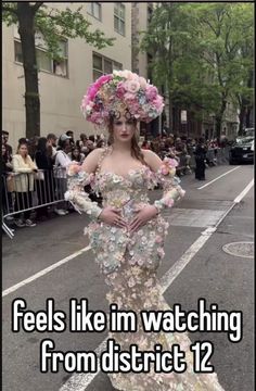 a woman in a dress with flowers on her head and the words feels like i'm watching from district 12