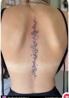 the back of a woman's neck with flowers and leaves tattooed on her lower back