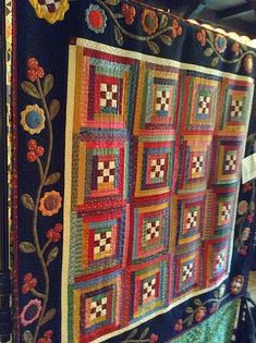 a colorful quilt hanging on the side of a wall next to a lamp and window