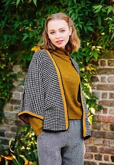 a woman standing in front of a brick wall wearing a black and white checkered jacket