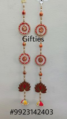 a pair of red and gold earrings hanging from a white wall with the words gifts on it