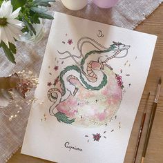 a card with a drawing of a dragon on it next to some flowers and candles