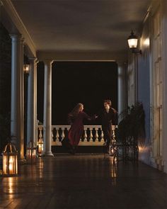 a man and woman walking down a porch at night with lanterns on either side of them