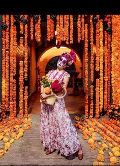 a woman standing in front of an archway with orange flowers on the wall and holding a basket