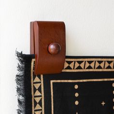 a close up of a rug hanging on a wall with a leather case attached to it