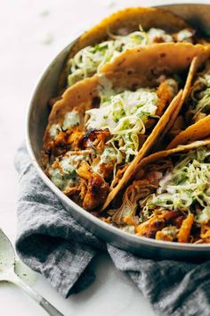 three tacos in a pan with shredded cabbage and other toppings on the side