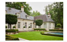 a large white house surrounded by lush green trees and bushes with a pool in the front yard