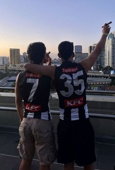 two young men standing on top of a roof with their arms around each other and pointing at the sky