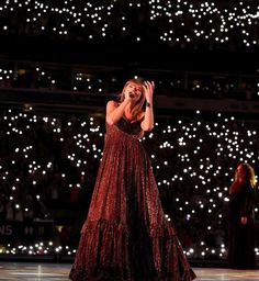 a woman in a long red dress on stage with her hand up to her face