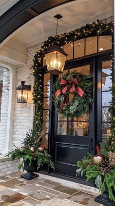 christmas wreaths are hung on the front door of a house decorated with lights and greenery