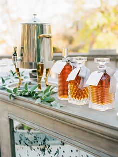 three bottles of honey sitting on top of a table next to a pot and silver kettle