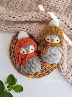 two crocheted penguins in hats and scarfs sitting on a basket next to a plant