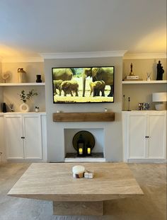 a flat screen tv mounted on the wall above a fireplace in a living room with white cabinets